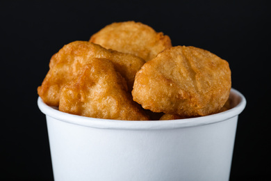 Photo of Bucket with delicious chicken nuggets on black background, closeup