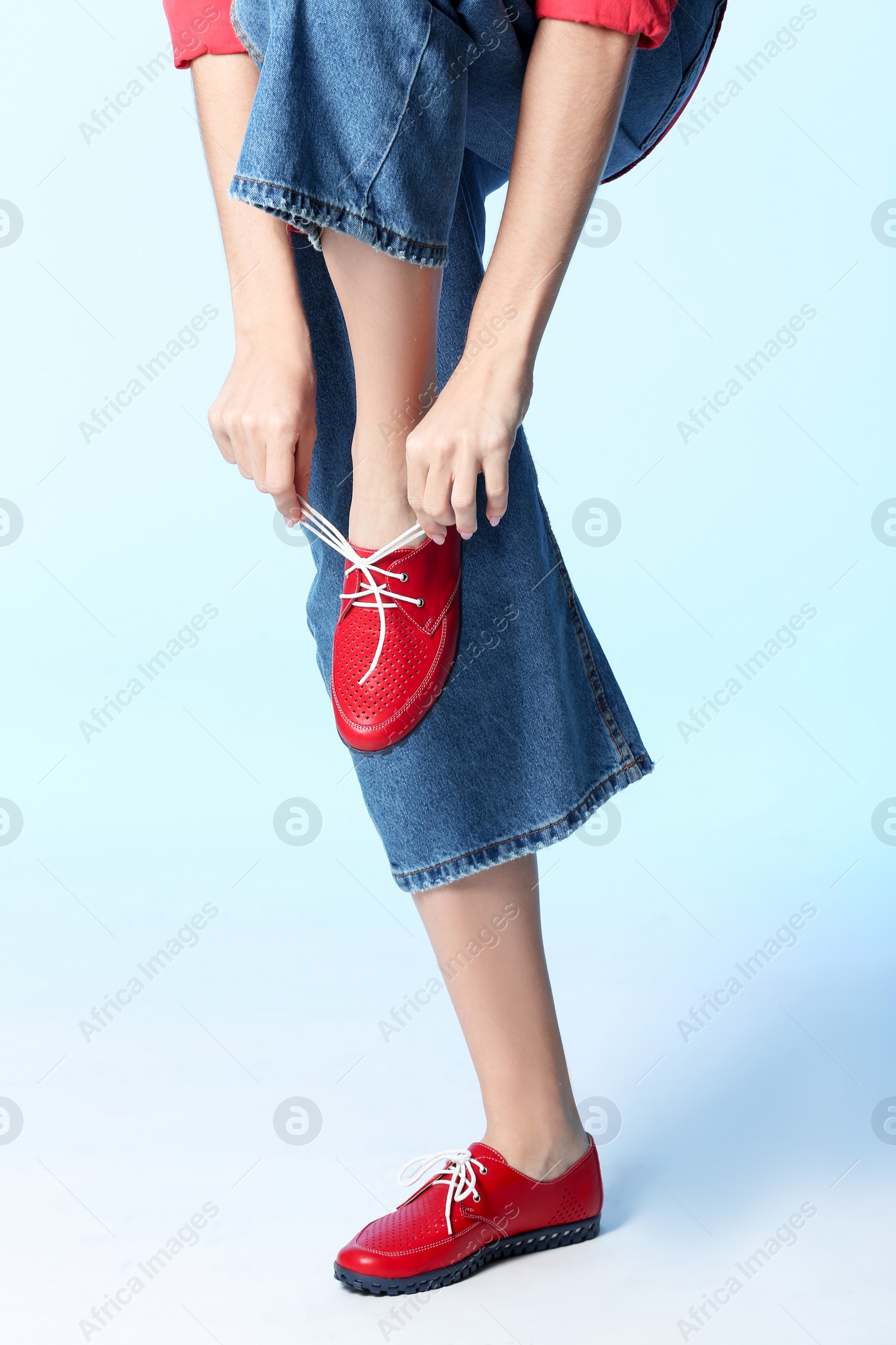 Photo of Woman tying laces of stylish shoe on color background, closeup