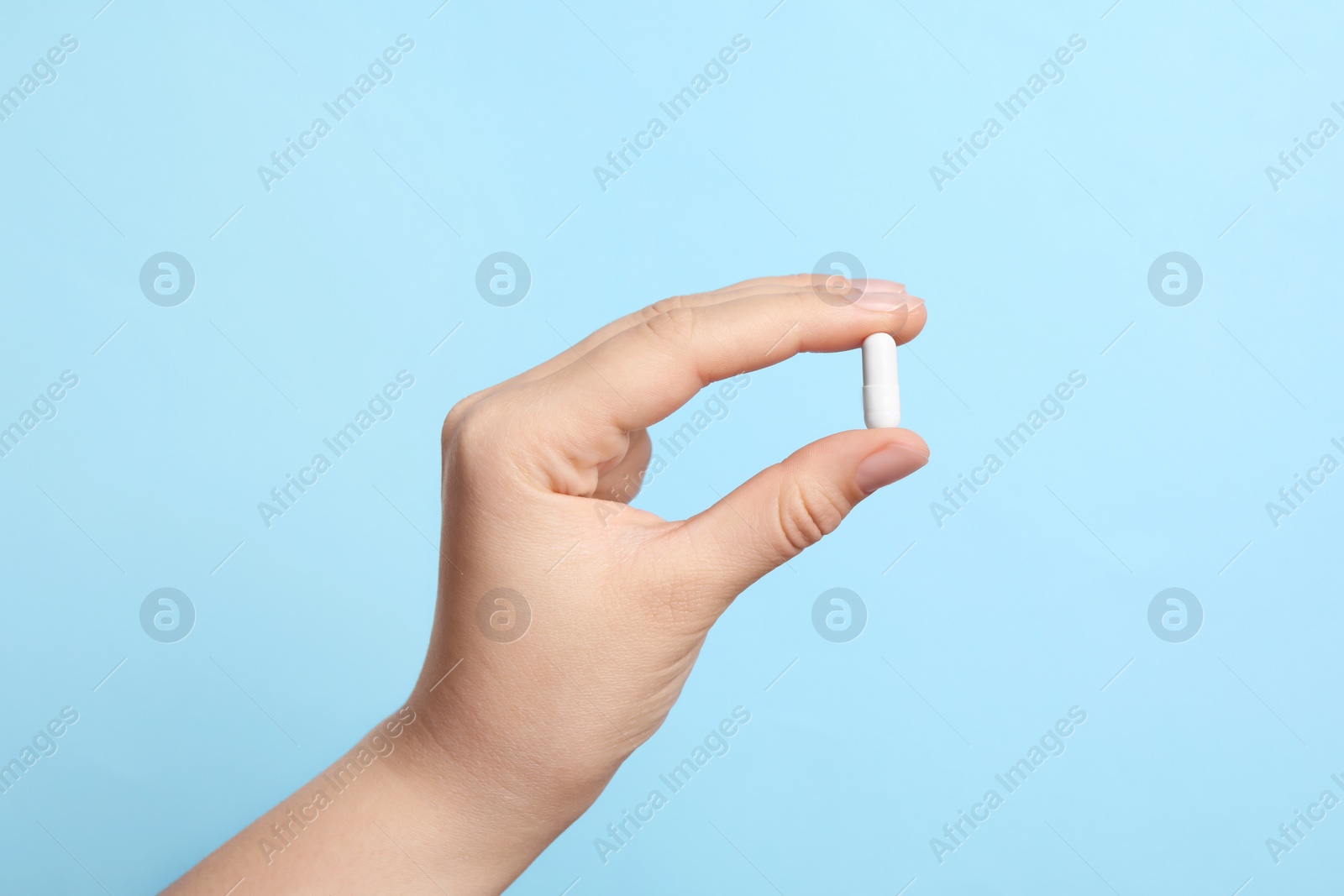 Photo of Woman holding pill on light blue background, closeup