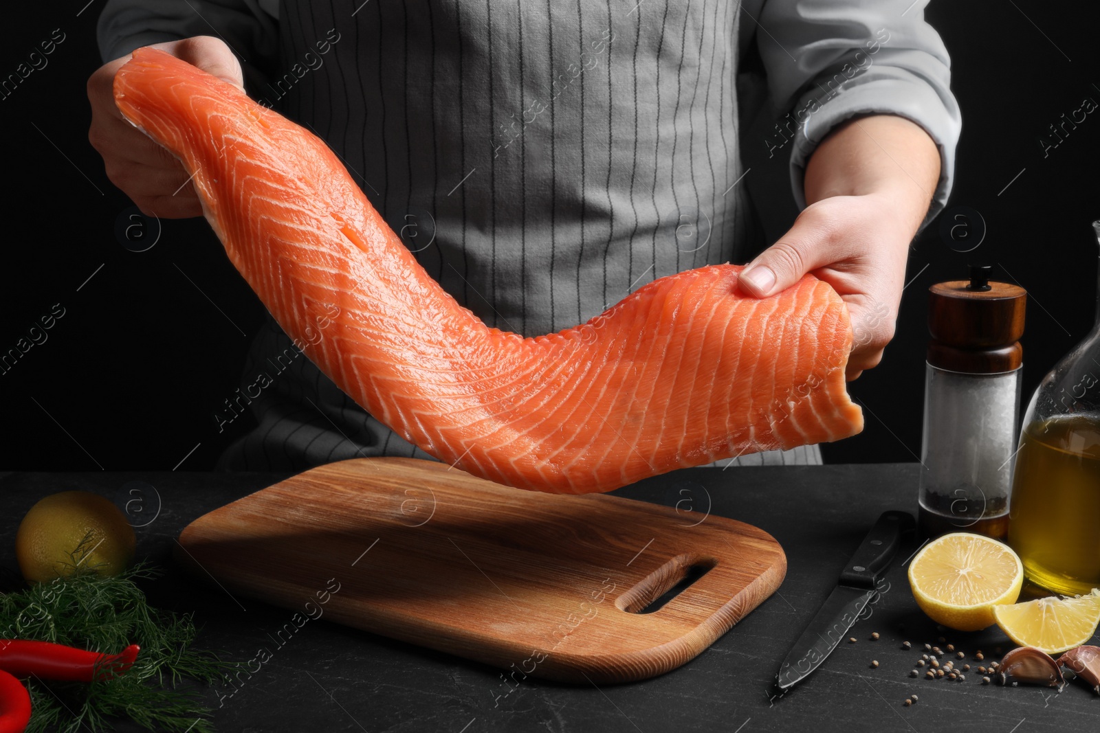 Photo of Man with raw salmon fillet at black table, closeup