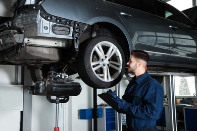 Technician checking car on hydraulic lift at automobile repair shop