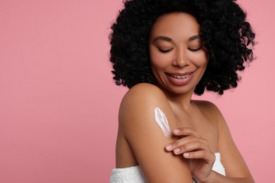 Photo of Young woman applying body cream onto shoulder on pink background. Space for text