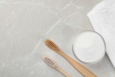 Photo of Bamboo toothbrushes, glass bowl of baking soda and towel on light grey marble table, flat lay. Space for text