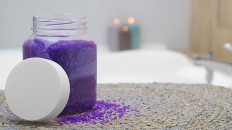 Photo of Jar with bath salt on wicker mat in bathroom. Space for text