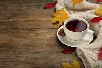 Cup of hot tea, sweater and autumn leaves on wooden table, space for text