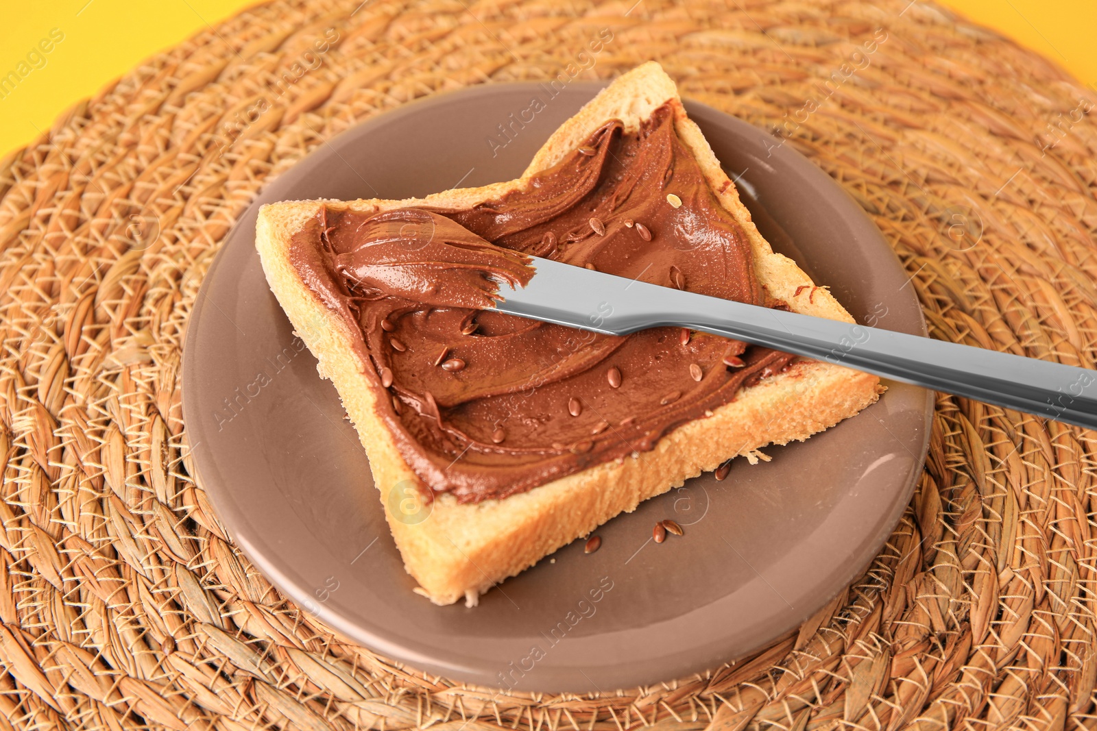 Photo of Spreading chocolate paste onto bread on yellow background, closeup