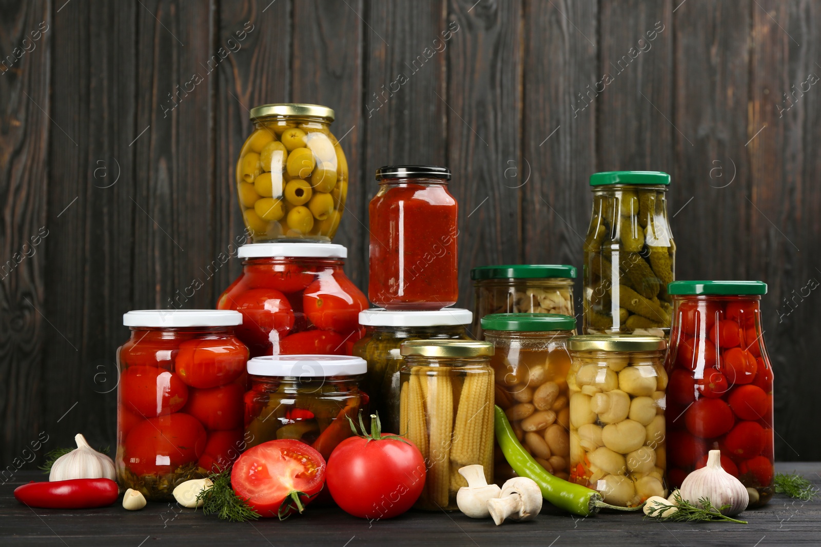 Photo of Glass jars with different pickled vegetables and mushrooms on wooden background