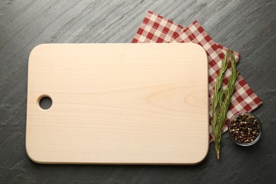 Photo of Wooden cutting board, spices and kitchen towel on dark grey table, flat lay