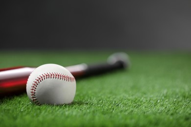 Photo of Baseball bat and ball on green grass against dark background, closeup. Space for text