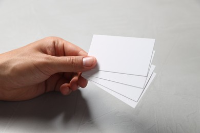 Man holding white blank cards at light grey table, closeup. Mockup for design