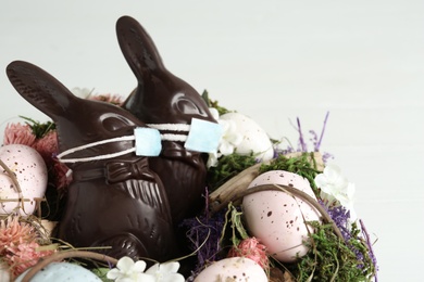 Photo of Chocolate bunnies with protective masks, eggs and wreath on white background, closeup. Easter holiday during COVID-19 quarantine