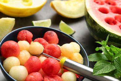 Bowl of melon and watermelon balls with scoop on table, closeup