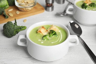 Photo of Delicious broccoli cream soup with croutons served on white wooden table