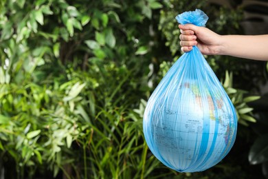 Photo of Woman holding globe in plastic bag against green leaves, closeup. Space for text. Environmental conservation