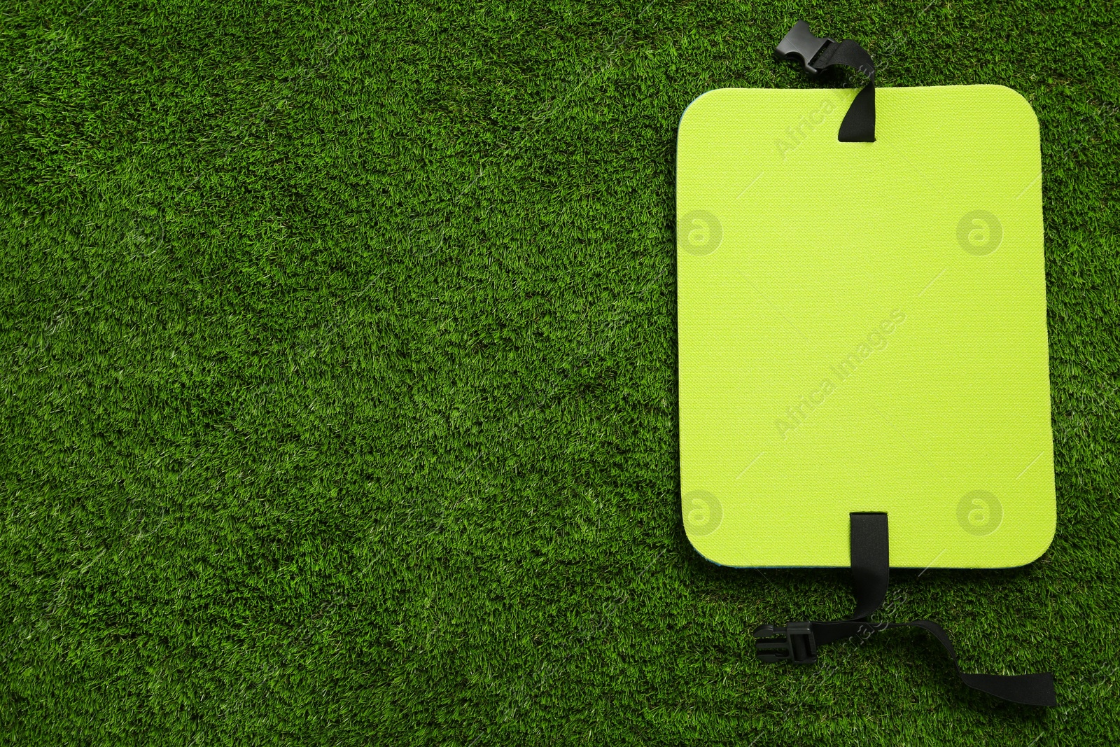 Photo of Bright foam tourist seat mat on green grass, top view. Space for text