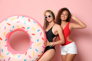 Beautiful young women in beachwear with inflatable ring on color background