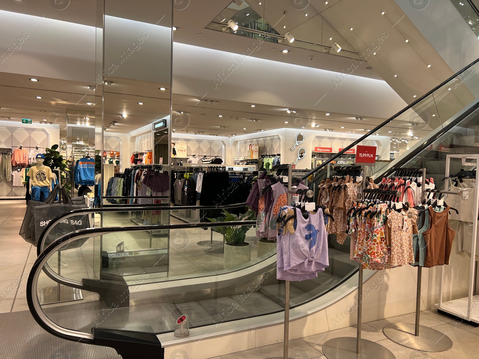 Photo of Racks with stylish clothes and escalator in shopping mall