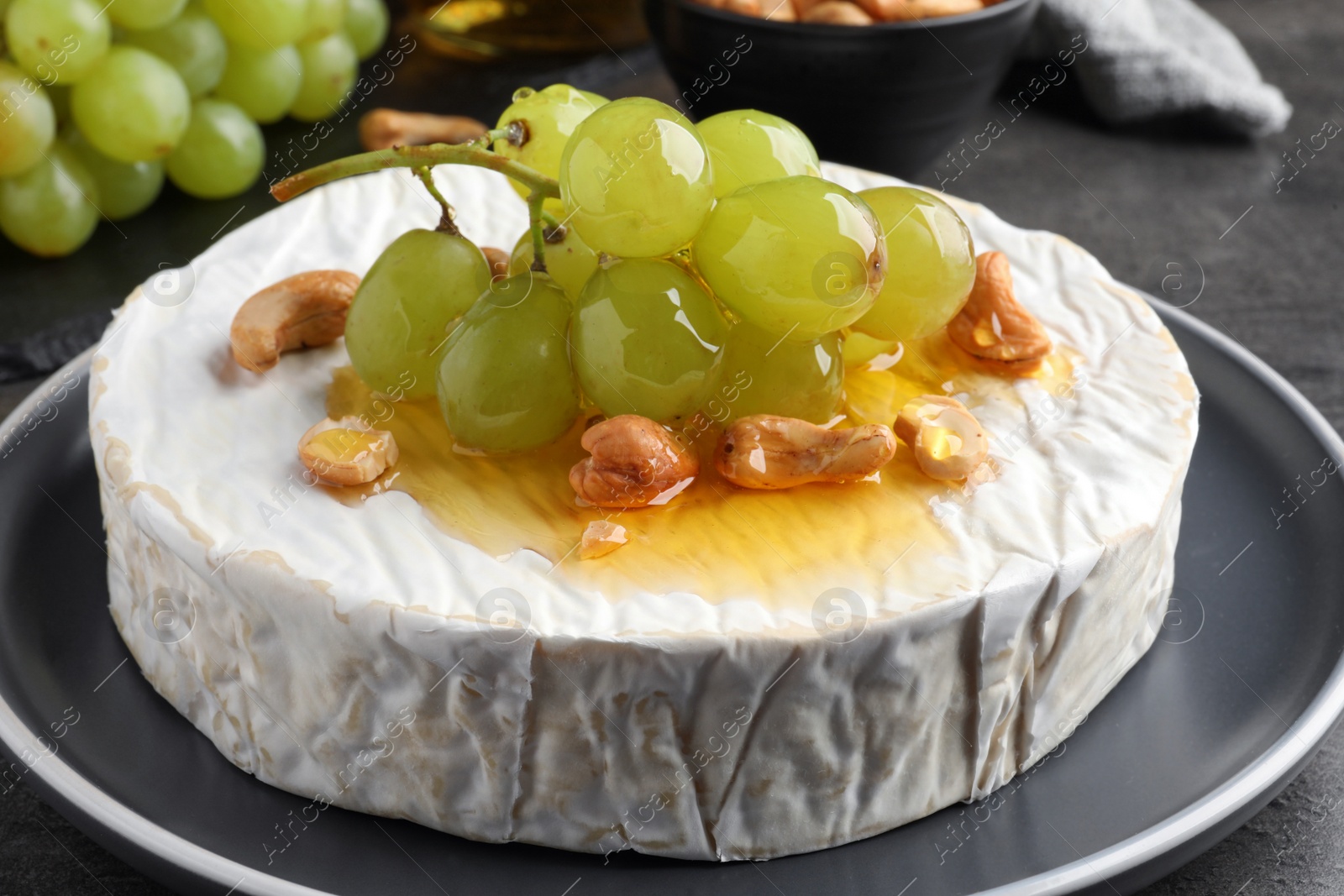 Photo of Brie cheese served with grape, cashew nuts and honey on dark grey table, closeup