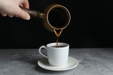 Photo of Turkish coffee. Woman pouring brewed beverage from cezve into cup at grey table, closeup