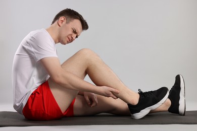 Man suffering from leg pain on mat against grey background