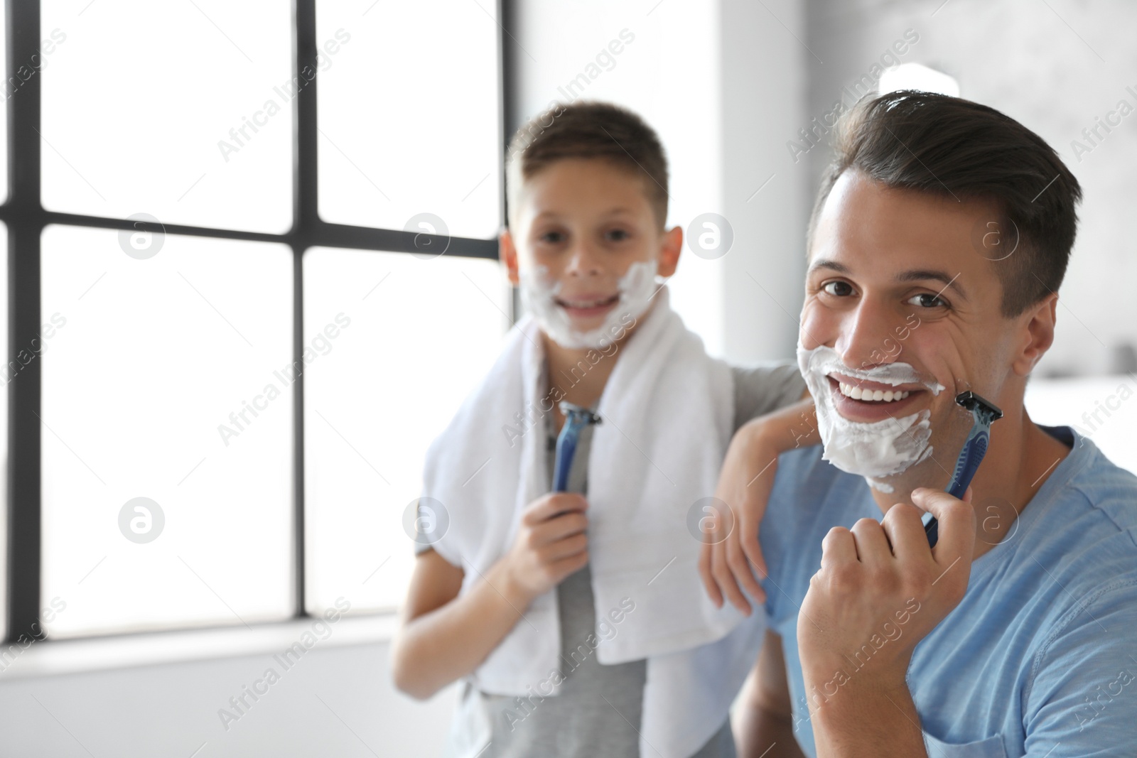 Photo of Happy father and son with shaving foam on their faces in bathroom