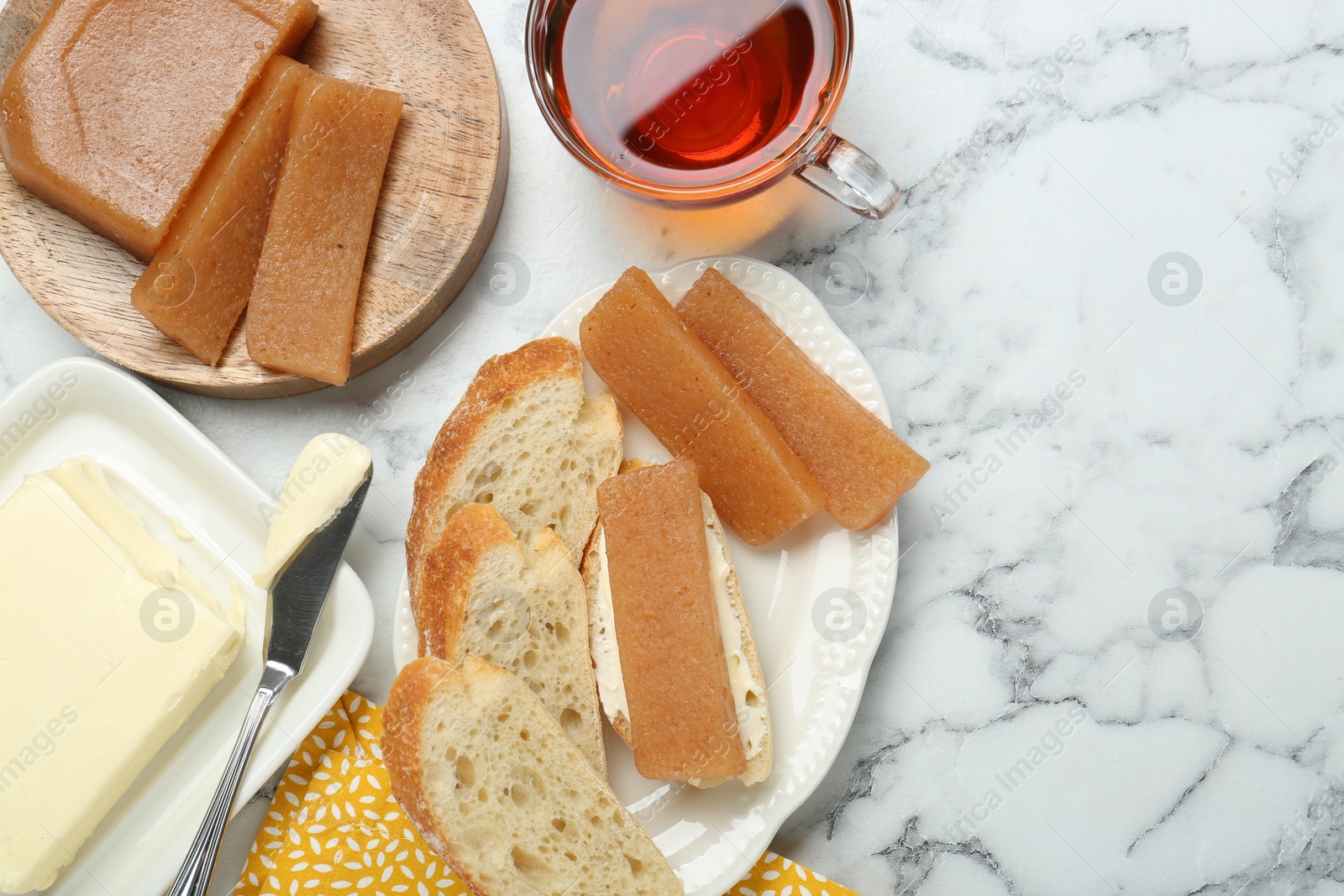 Photo of Delicious quince paste, bread, butter and cup of tea on white marble table, flat lay. Space for text