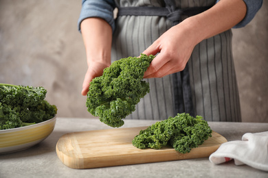 Photo of Woman holding fresh kale leaves over light grey table, closeup