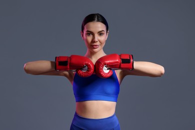 Portrait of beautiful woman wearing boxing gloves in color lights on grey background