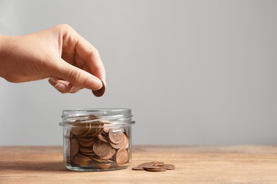 Photo of Woman putting coin in glass jar with money at wooden table, closeup. Space for text