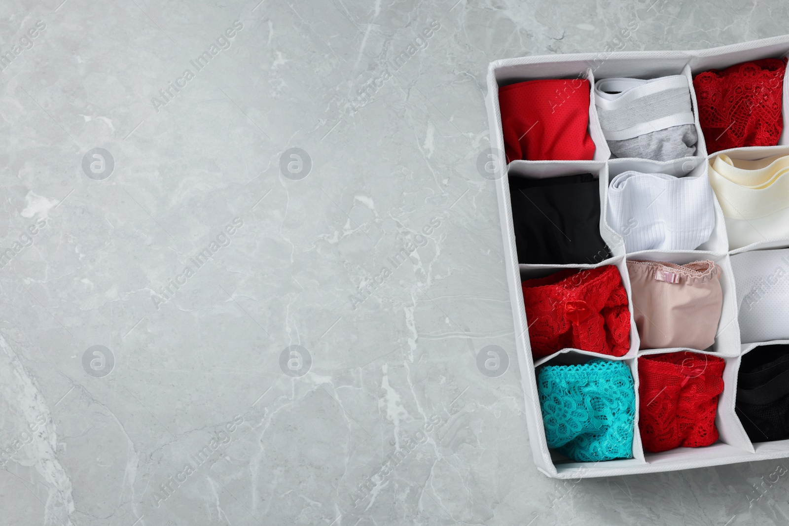 Photo of Organizer with folded women's underwear on light grey marble table, top view. Space for text