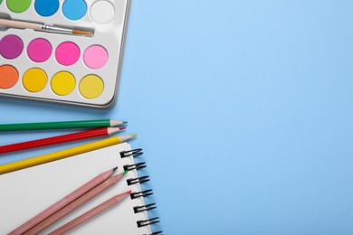 Photo of Watercolor palette, colorful pencils and notebook on light blue background, flat lay. Space for text