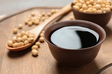 Photo of Bowl of soy sauce and beans on wooden board, closeup