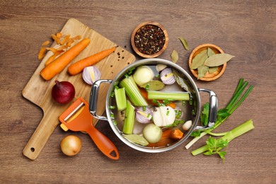 Photo of Pot and different ingredients for cooking tasty bouillon on wooden table, flat lay