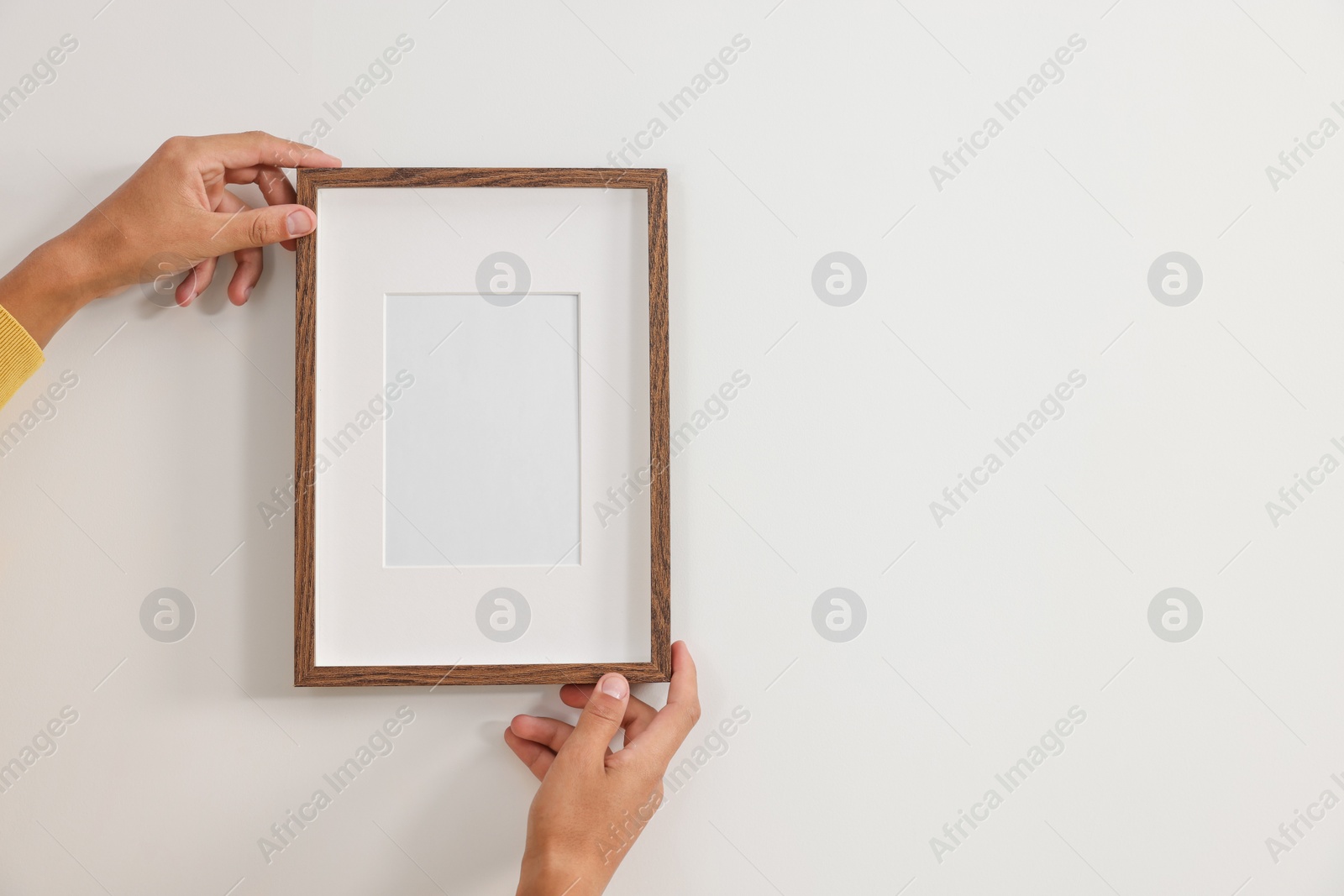 Photo of Young man hanging picture frame on white wall indoors, closeup. Space for text