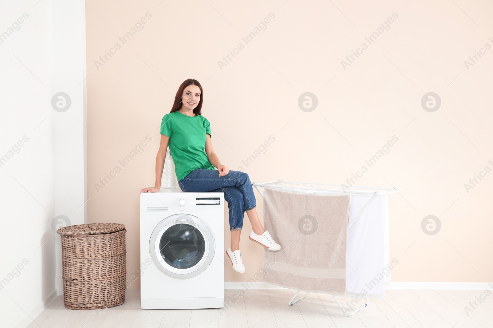 Photo of Young woman sitting on washing machine at home, space for text. Laundry day