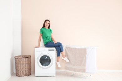 Photo of Young woman sitting on washing machine at home, space for text. Laundry day