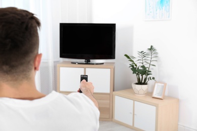 Photo of Young man switching channels on modern TV with remote control at home