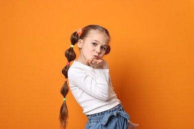 Photo of Cute little girl with beautiful hairstyle blowing kiss on orange background