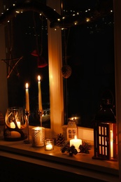 Photo of Burning candles and Christmas decor on window sill at night