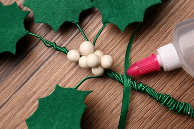 Photo of Handmade mistletoe branch, green ribbon and glue on wooden table, closeup
