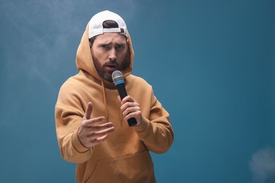 Photo of Singer in hoodie with microphone rapping on light blue background. Space for text