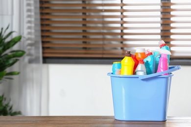 Photo of Plastic bucket with different cleaning products on table indoors, space for text