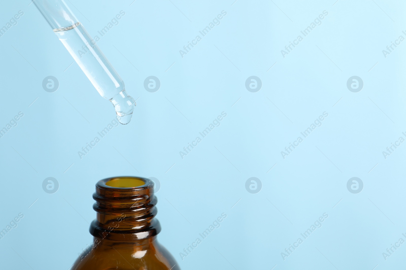 Photo of Dripping cosmetic serum from pipette into bottle on light blue background, space for text