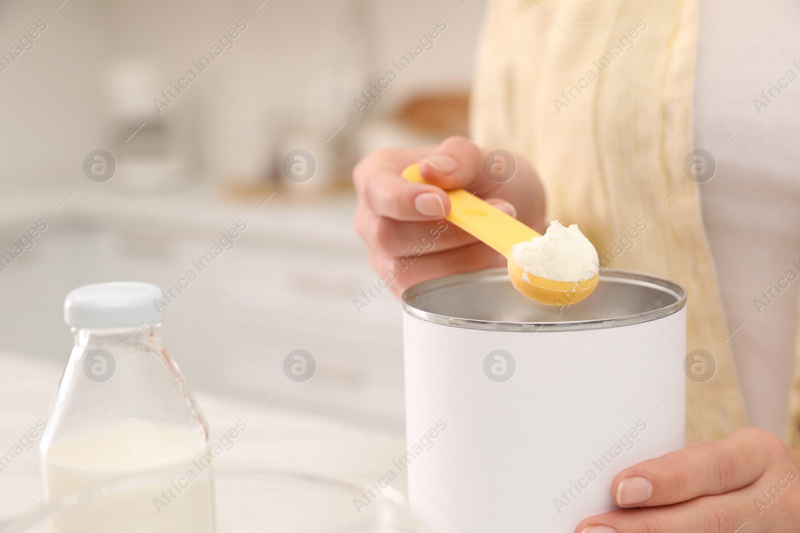 Photo of Woman preparing infant formula at table indoors, closeup. Baby milk