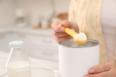 Photo of Woman preparing infant formula at table indoors, closeup. Baby milk