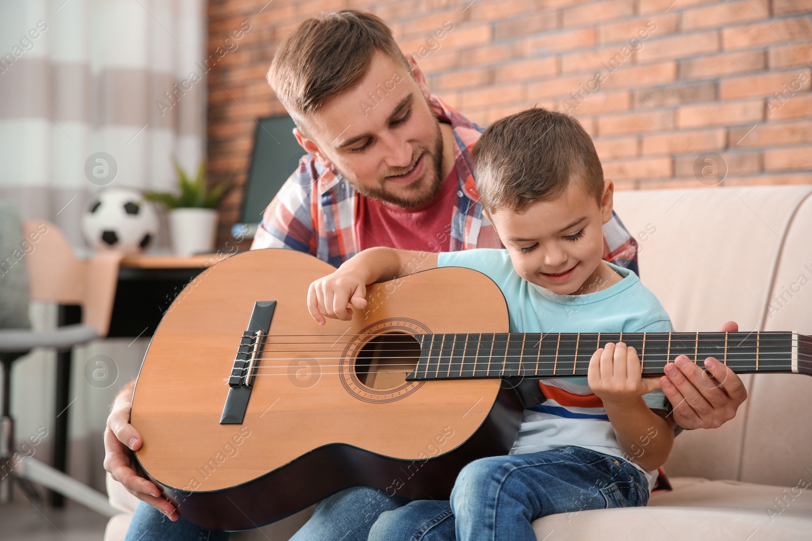 Photo of Father teaching his little son to play guitar at home