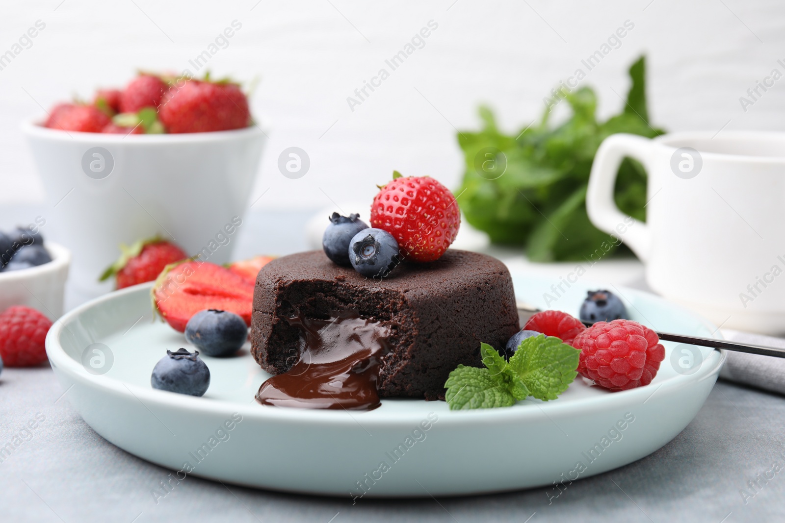 Photo of Plate with delicious chocolate fondant, berries and mint on grey table, closeup