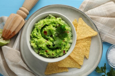Photo of Delicious guacamole served with nachos chips on light blue table, flat lay