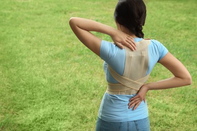 Photo of Woman with orthopedic corset on green grass outdoors, space for text