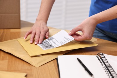 Photo of Parcel packing. Post office worker sticking barcode on bag at wooden table indoors, closeup